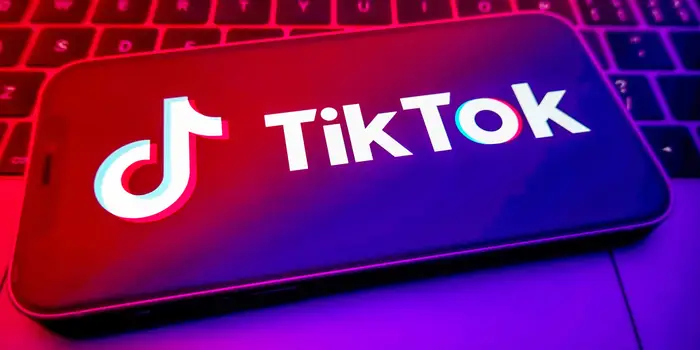 The TikTok logo is displayed on a smartphone screen, illuminated with vibrant red and purple lighting, and placed on a keyboard background.