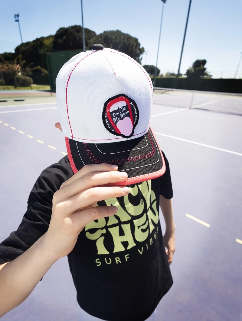 Casquette blanche The Prompt Factory mise en avant lors d’un shooting sur un court de tennis