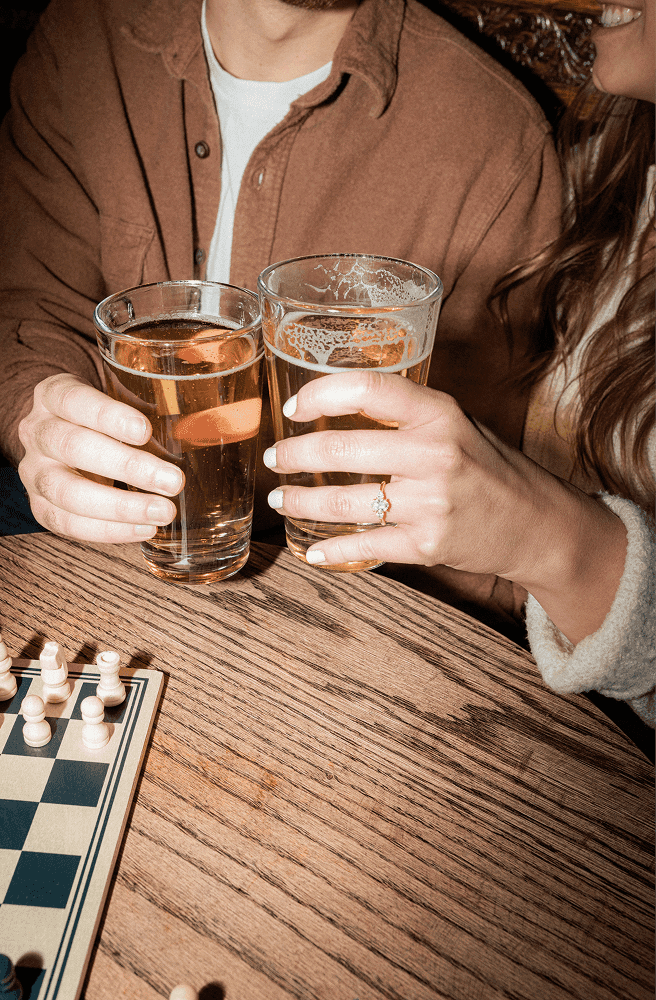 two people clinking beer glasses, which only their hands and torsos visible