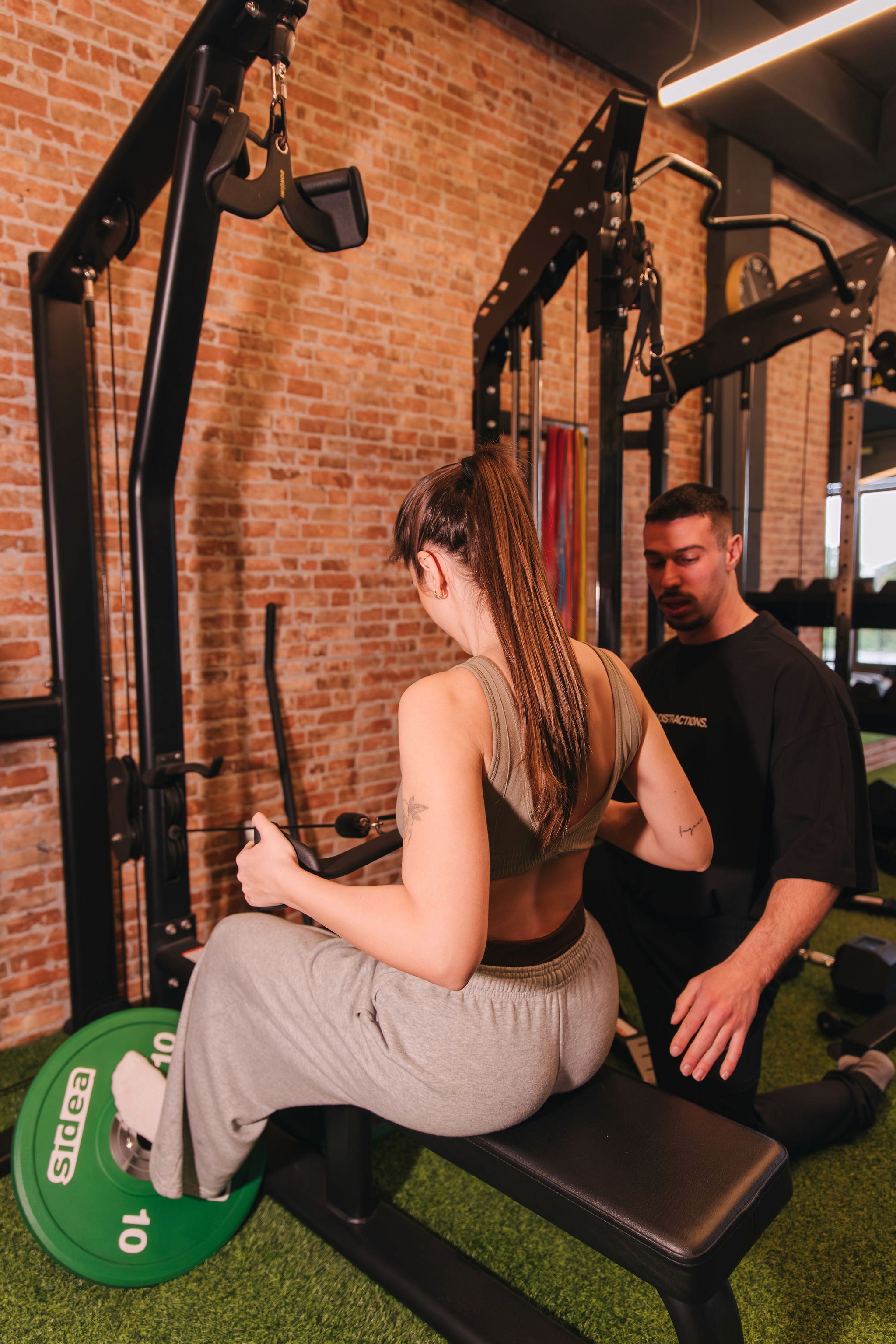 Cliente realizando ejercicio en polea con supervisión de entrenador en La Base Strength, Sitges