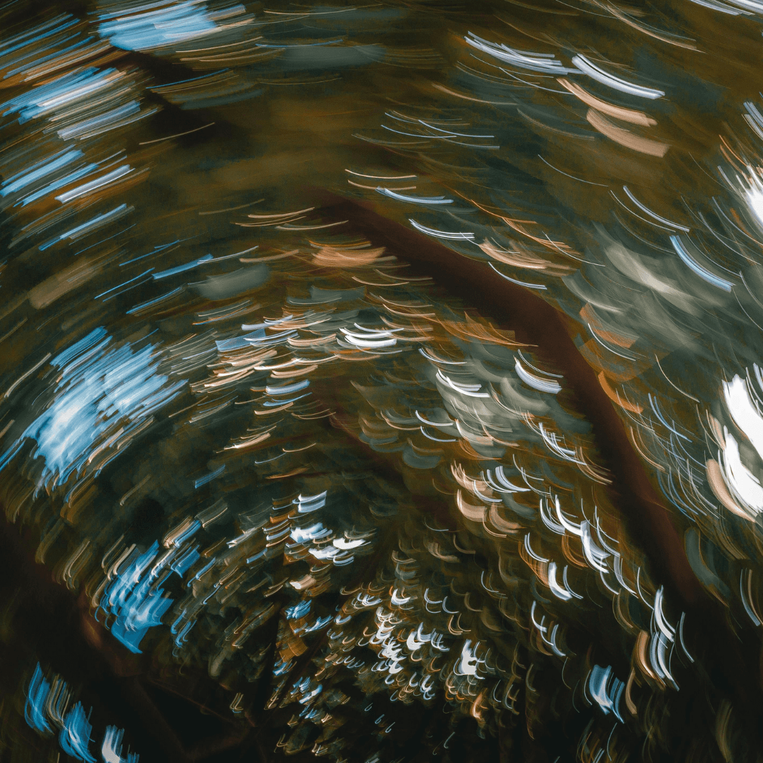 Una persona con una camiseta negra y pantalones de color claro está de pie en la cima rocosa de una montaña al atardecer, sosteniendo una cámara frente a su cara para tomar una foto. Un mar de nubes se extiende detrás de ellos, iluminado por la luz dorada del sol poniente.