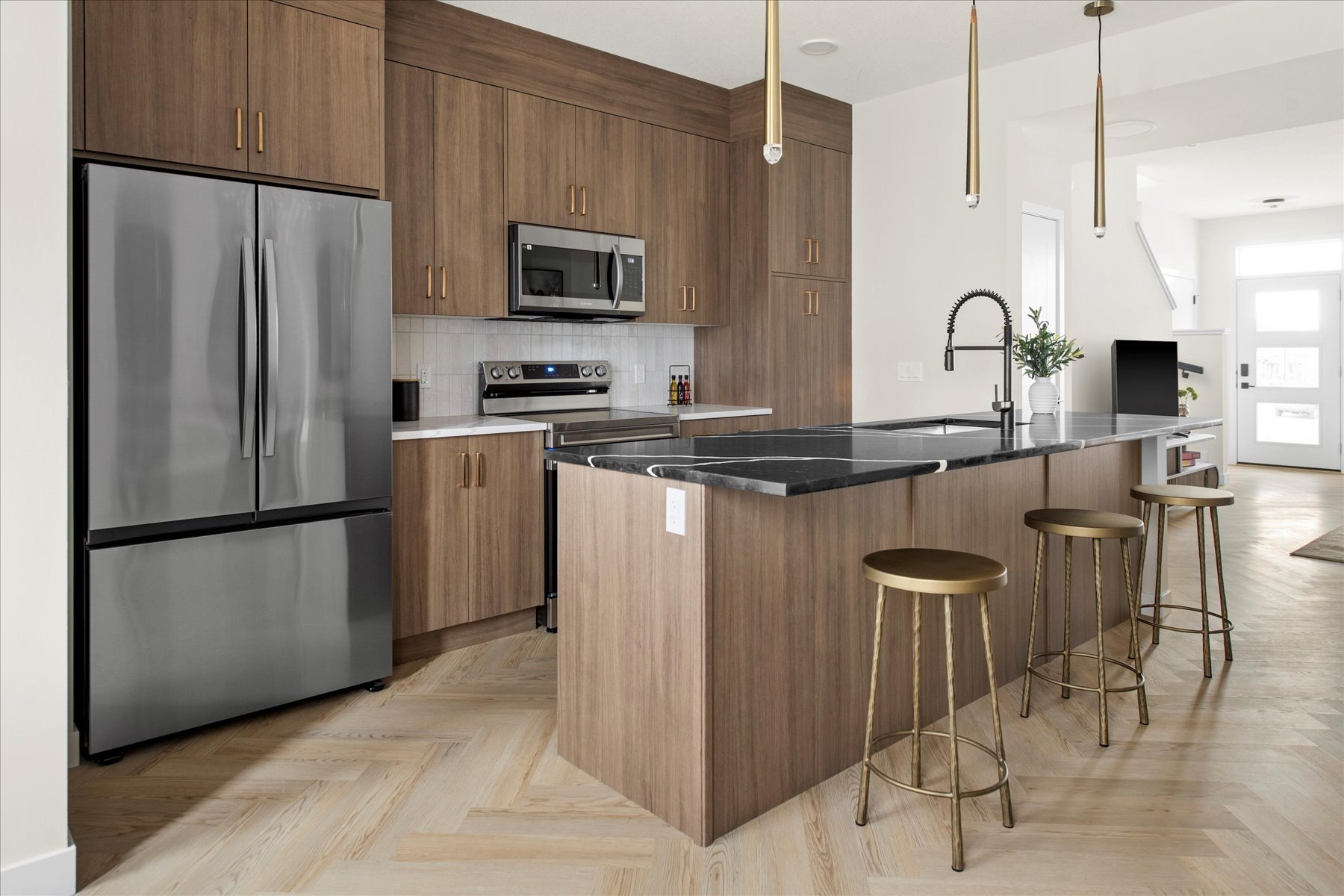 Heartland show suite kitchen finished: wood-grain cabinetry, black counters, brass stools and herringbone floor