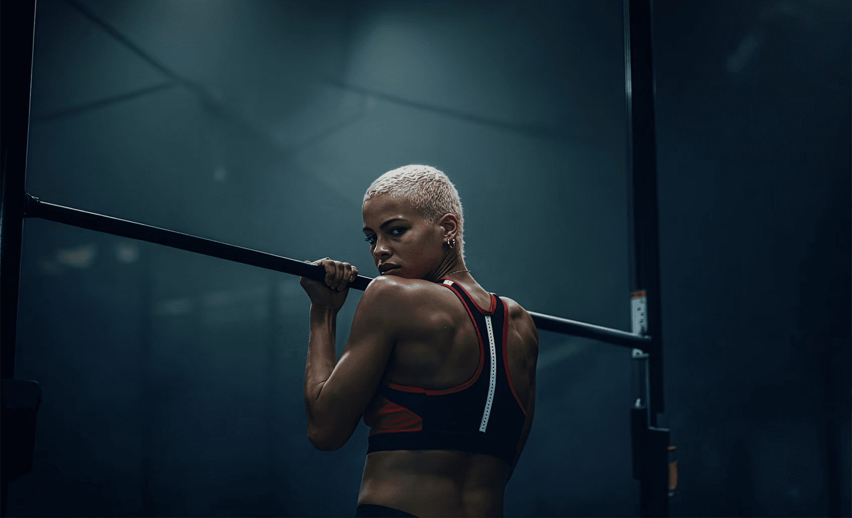 Fit woman with short blonde hair on a pull-up bar, looking over shoulder.