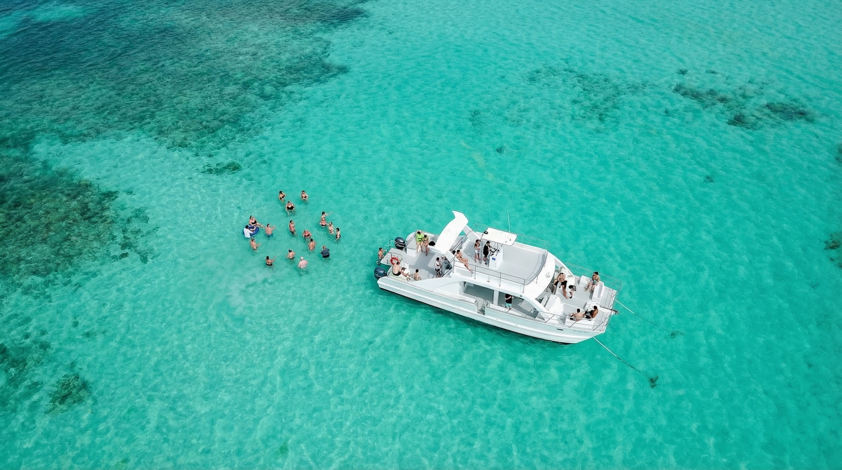 Aerial view of people swimming near a white boat in clear turquoise water