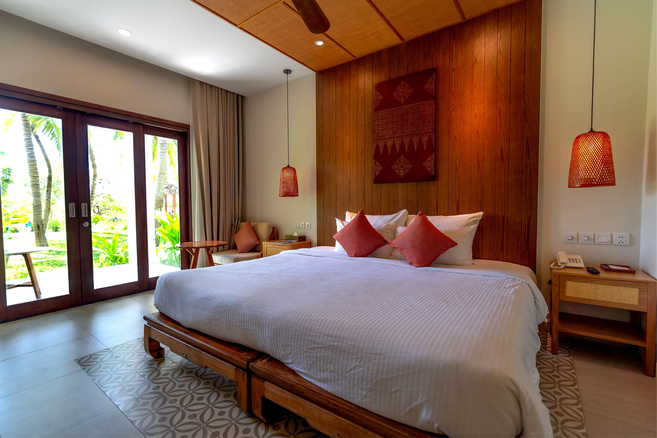 Deluxe pool view room with a large bed, warm wooden details, and red accent pillows.