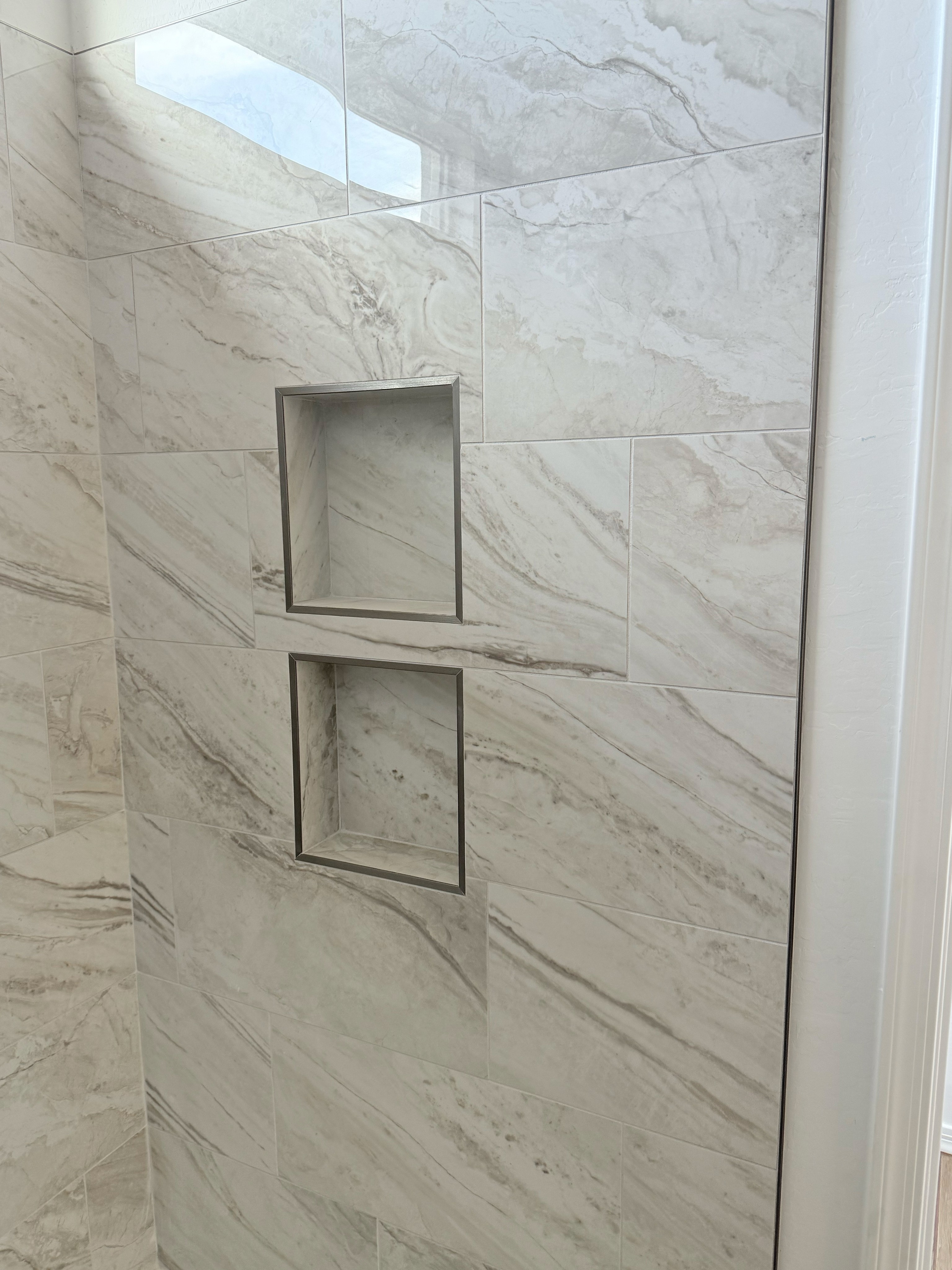 Modern shower wall tiled with large light brown marble-look tiles featuring two built-in rectangular shower niches.