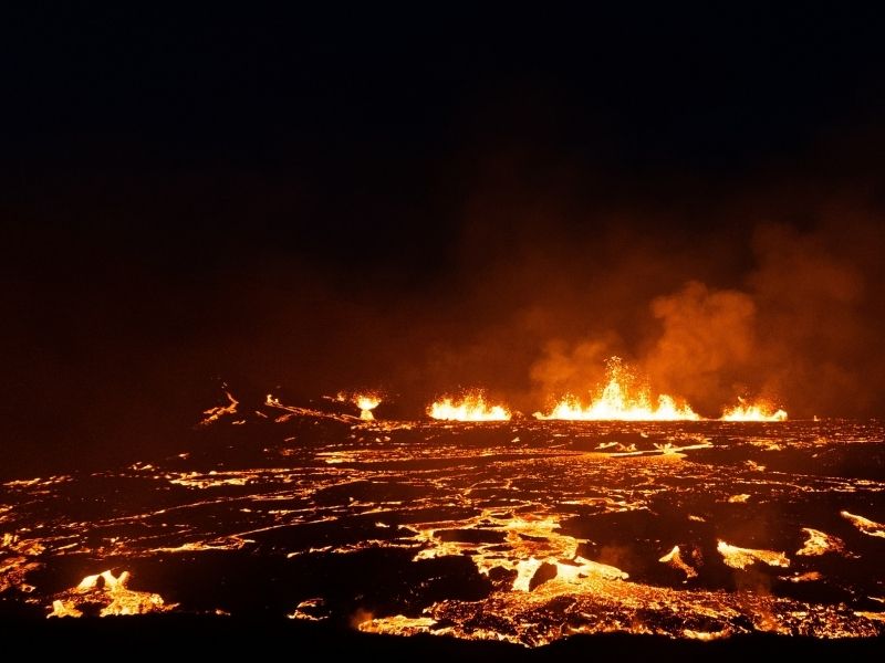 Bright orange lava flowing across a dark volcanic landscape at Fagradalsfjall in Iceland during an effusive eruption at night.