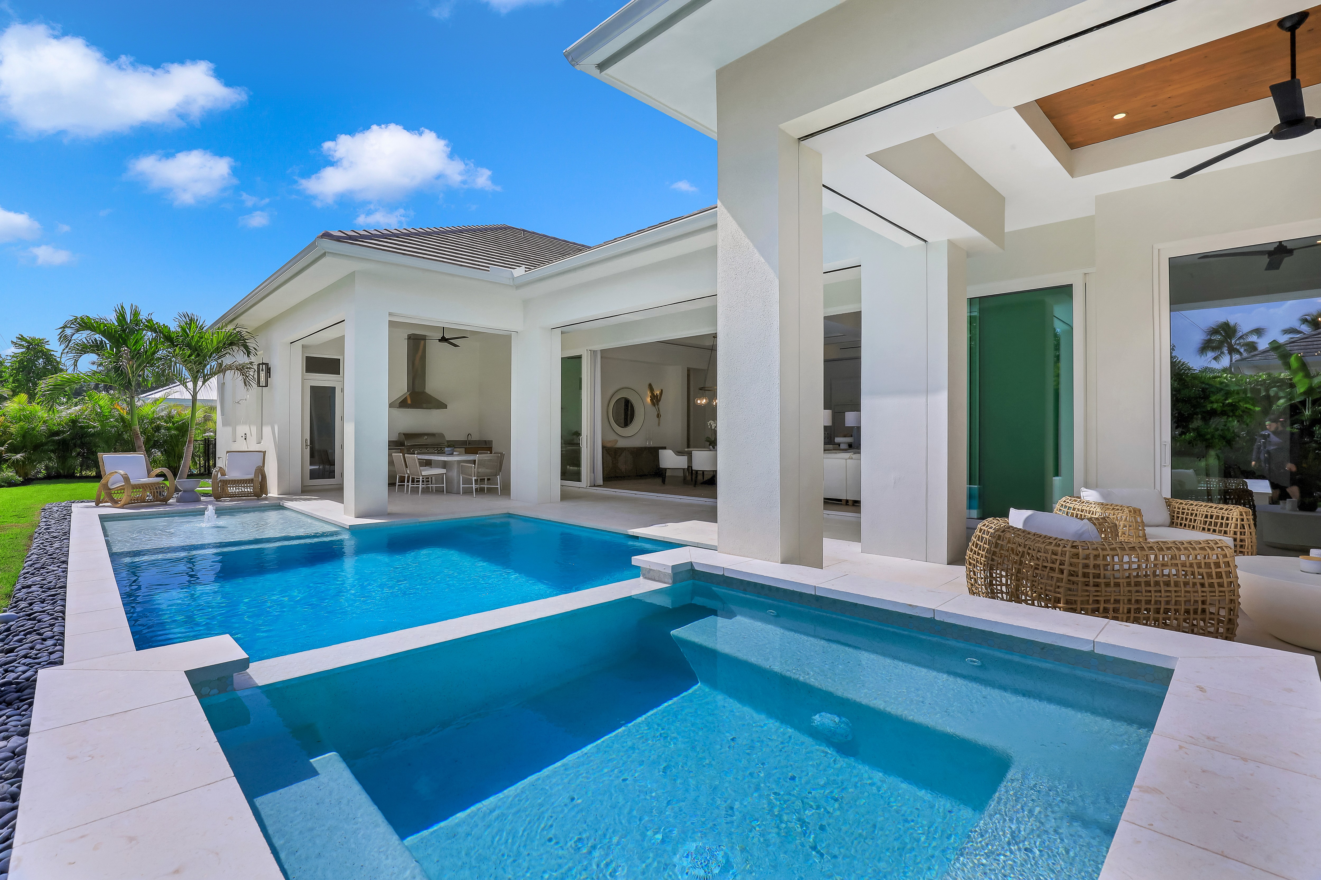 a large pool surrounded by luxurious white tile and white pillars leading into a modern home