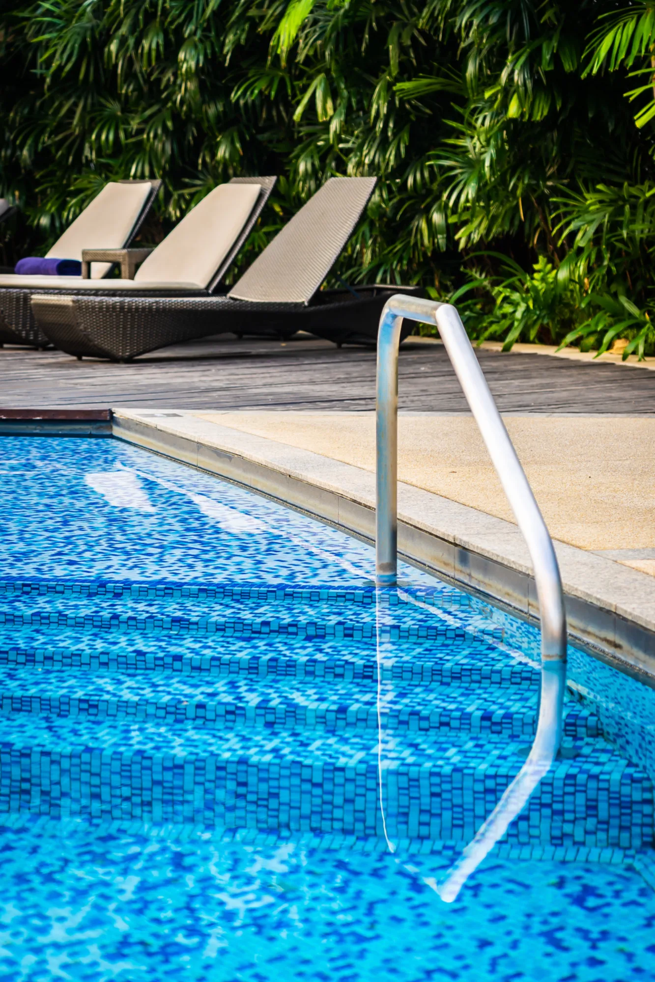 Stainless steel pool handrail beside a bright blue swimming pool.