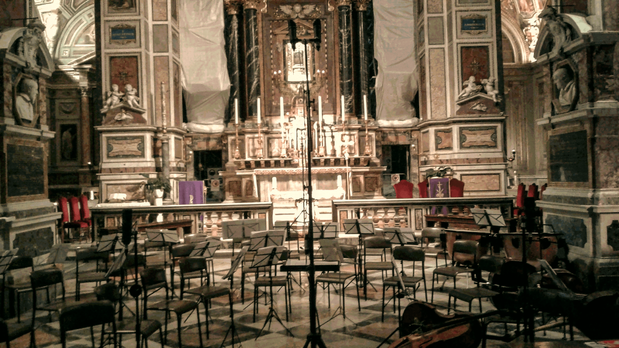 Interno di una chiesa allestito per una registrazione, con microfoni, leggii, sedie e strumenti.