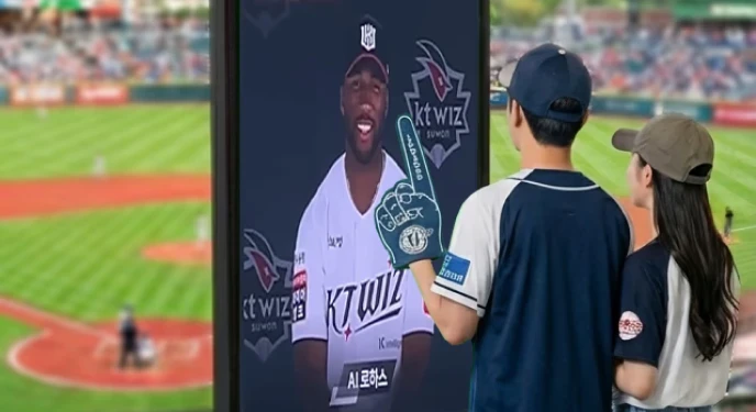 A woman in a white suit stands confidently against a bright red background, smiling with one hand on her hip.