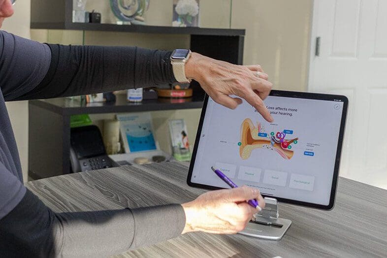 A person points at a computer monitor displaying a colorful graphic design in a modern workspace.