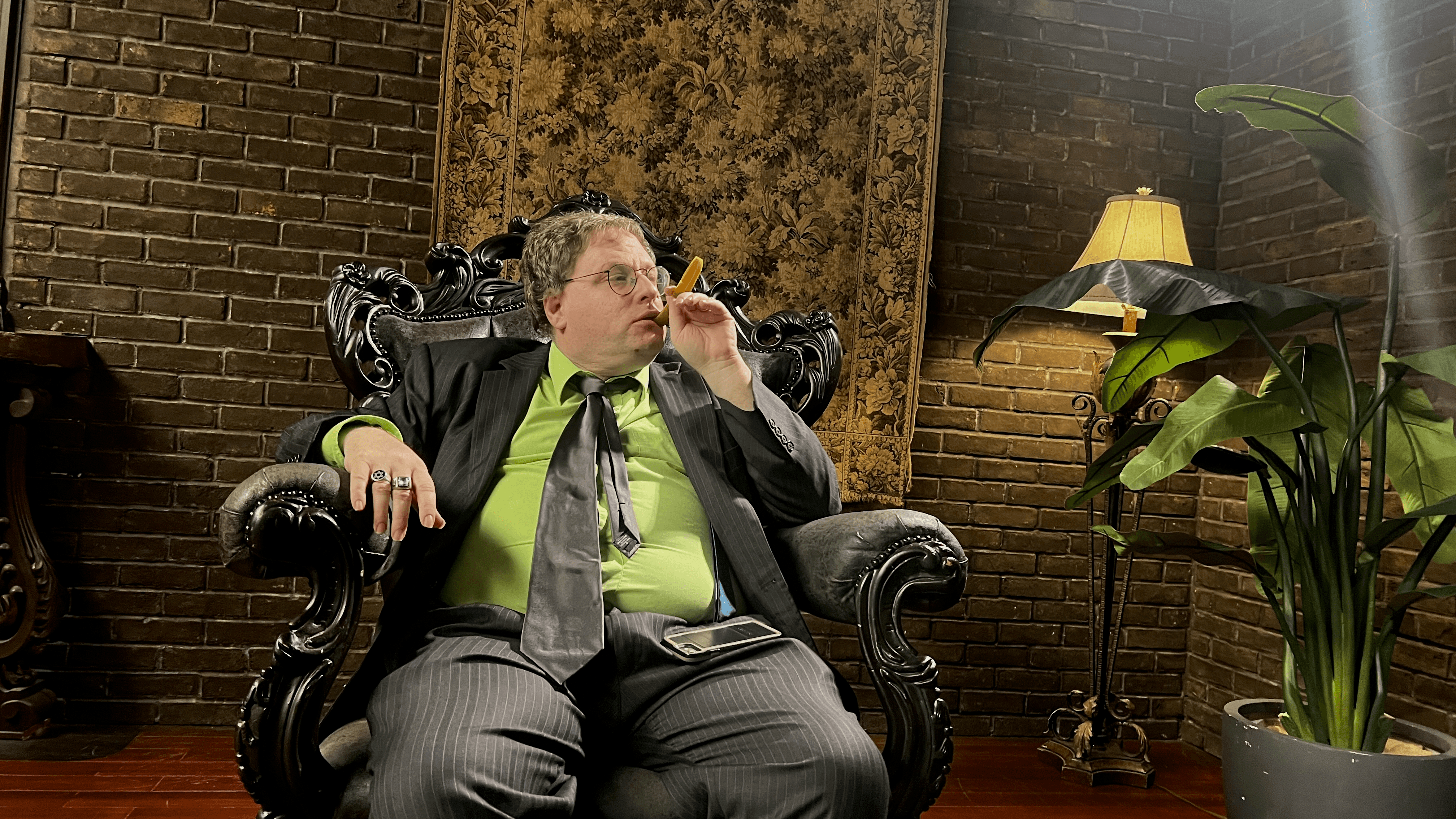 Host in the throne chair with a pickle cigar on the library set