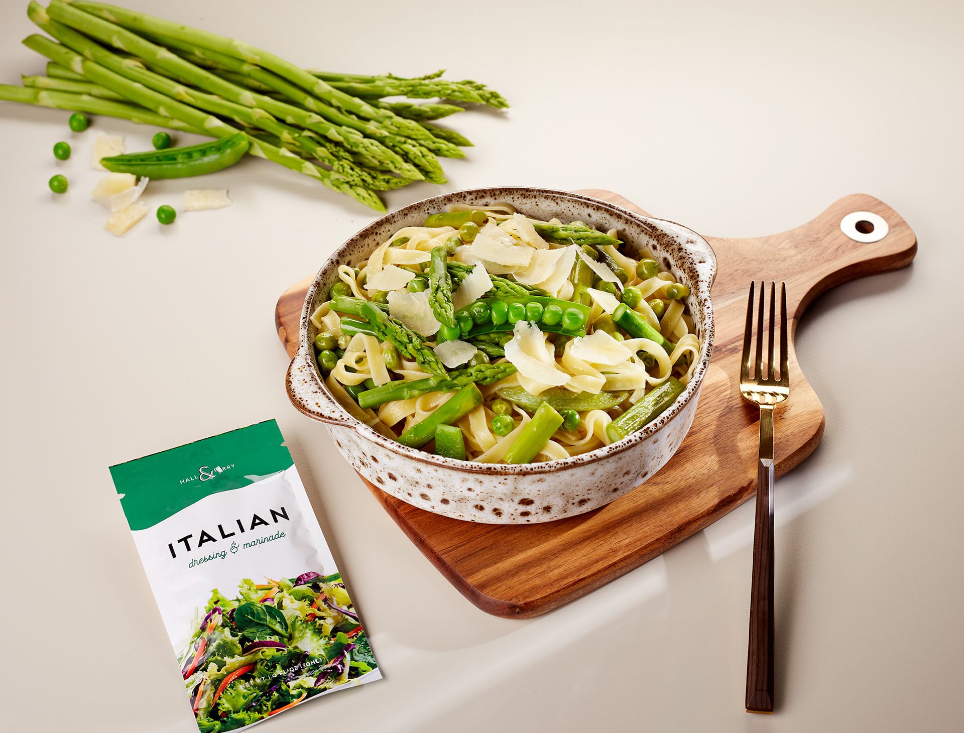 A vibrant bowl of fresh green pasta topped with asparagus and peas, displayed on a wooden cutting board alongside a package of Italian Pocket Flavors seasoning blend.