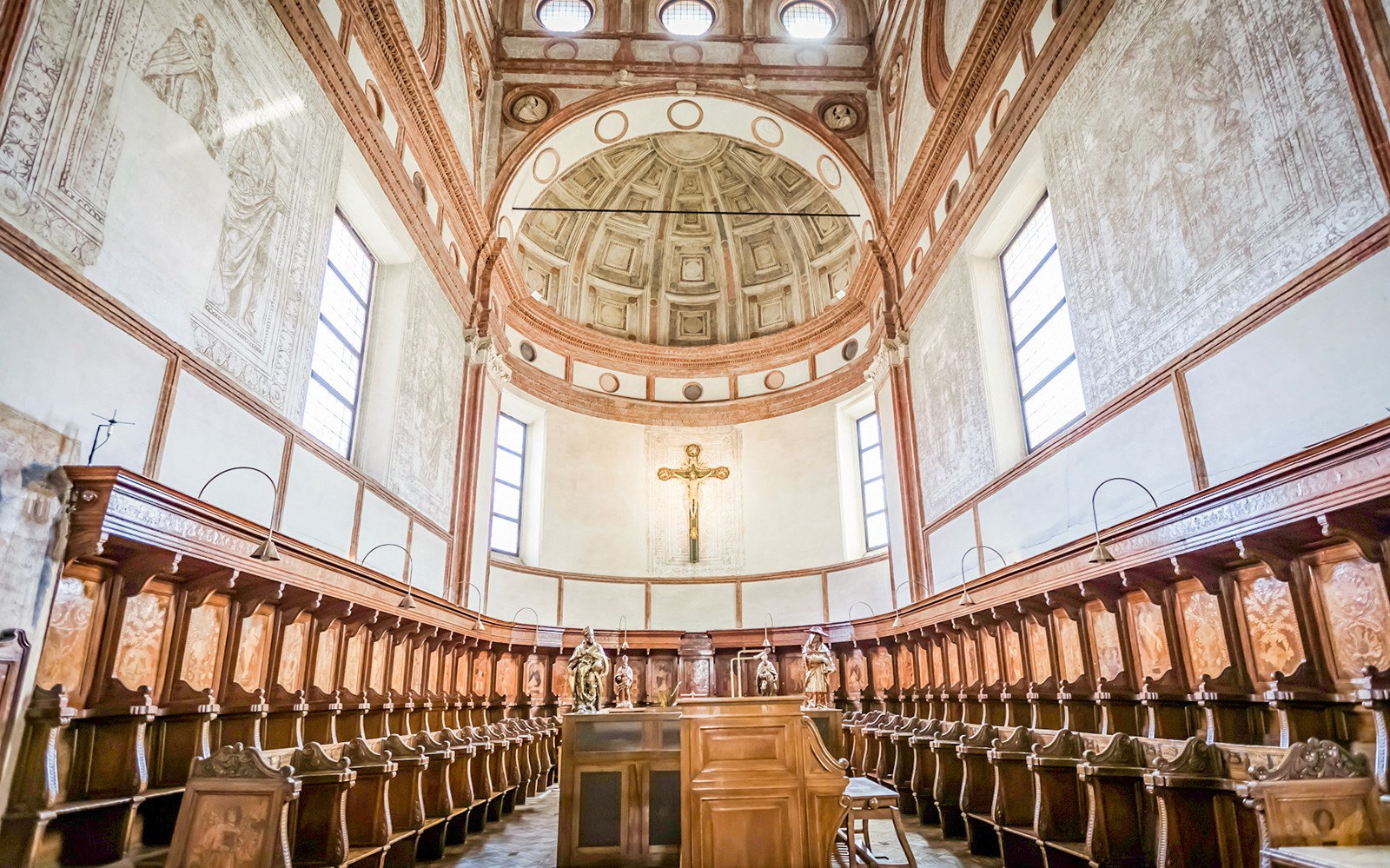 Innanrými Santa Maria delle Grazie kirkjunnar með viðarkórbekkjum og krossi.