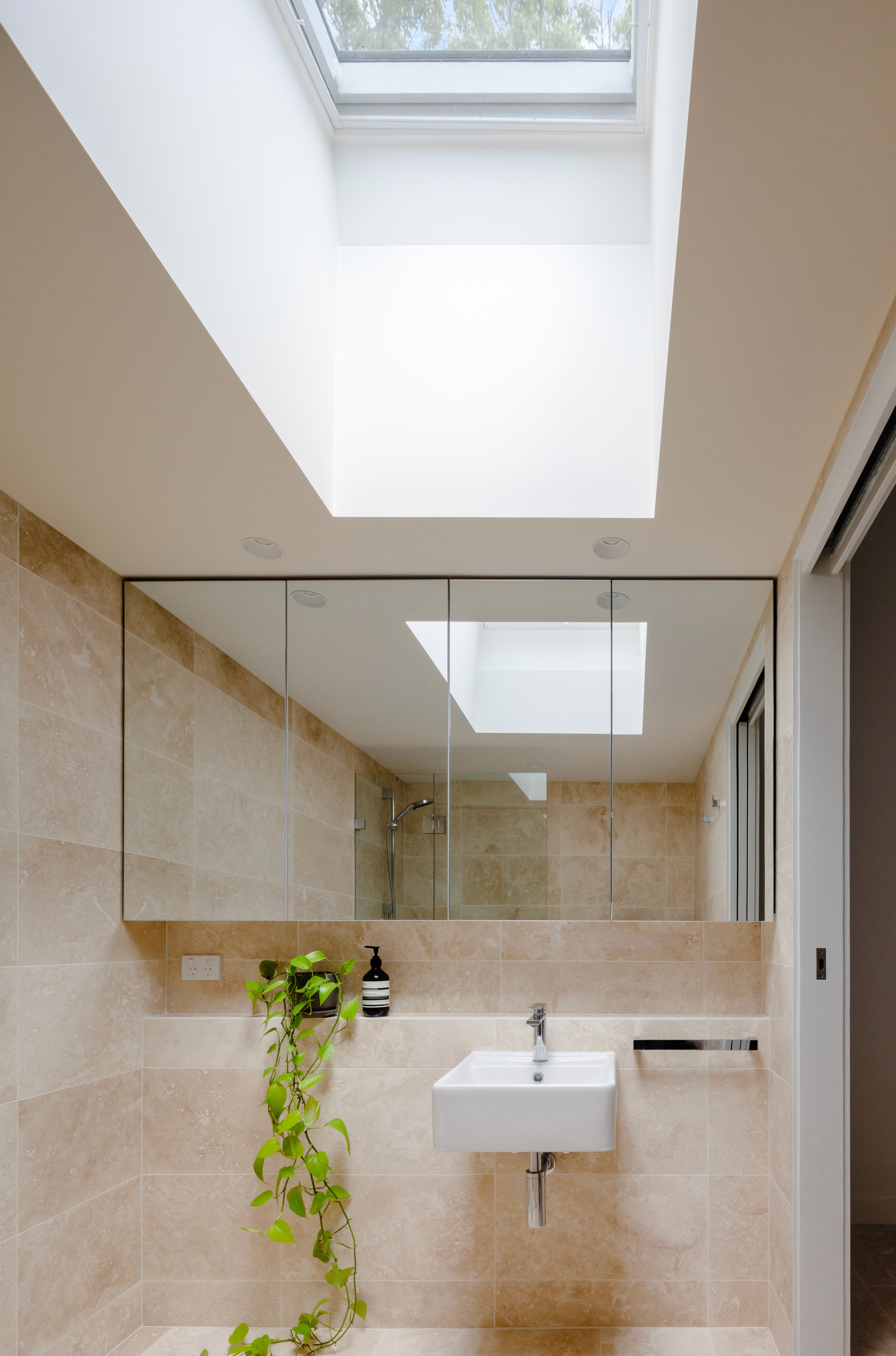 Bathroom interior featuring travertine finishes, a skylight bringing daylight deep into the space, and a pared-back, functional layout.