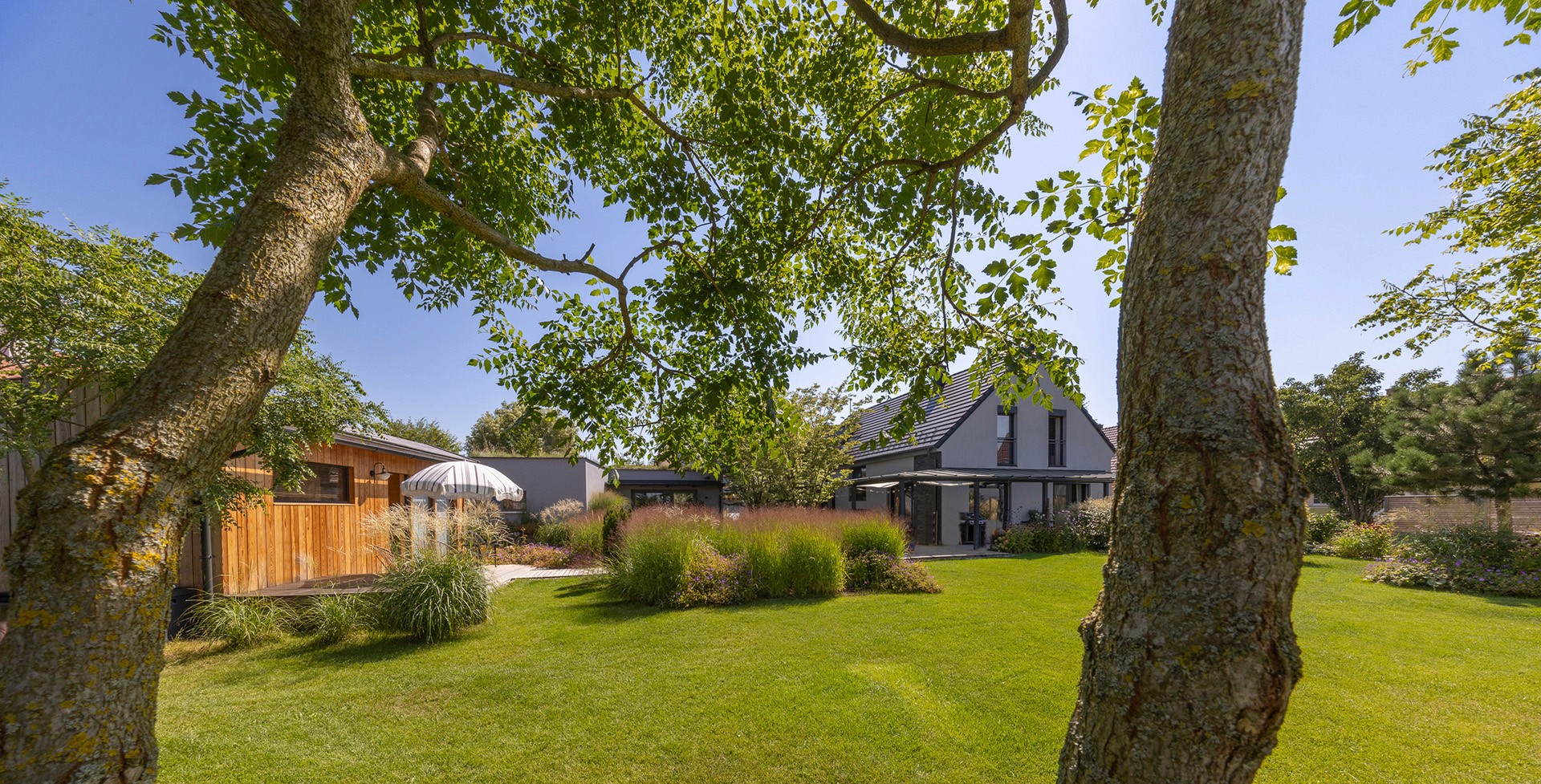 Großzügiger Garten mit Rasenfläche, naturnahen Staudenbeeten und schattenspendenden Bäumen.