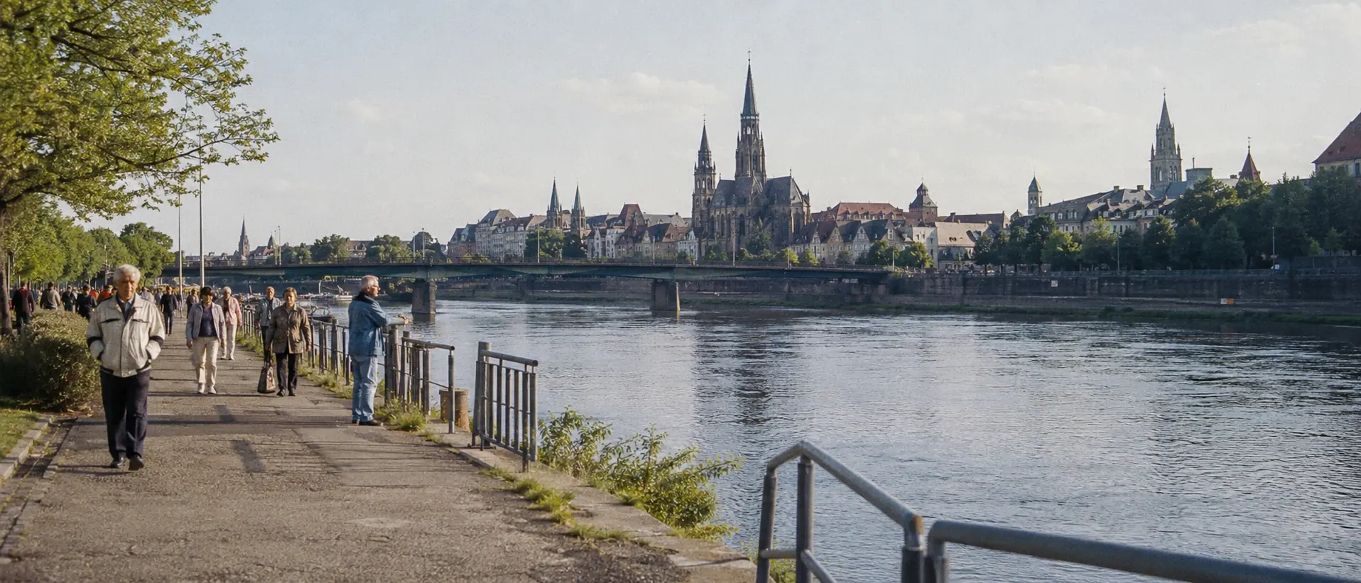 Stadtpromenade an Elbe oder Saale mit Domspitzen und Spaziergängern im Morgenlicht