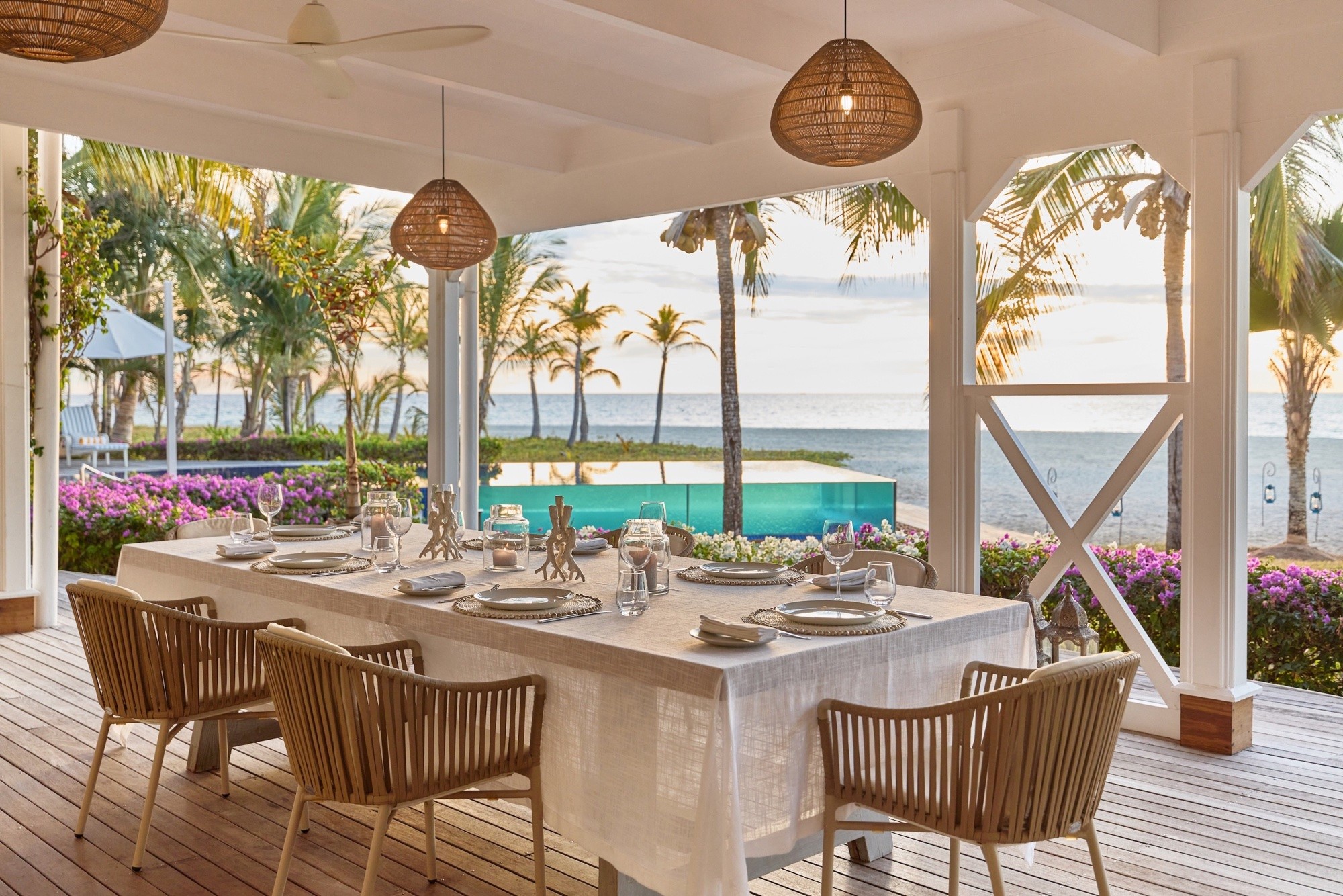 A beach-house veranda set for dinner beside palms and sea