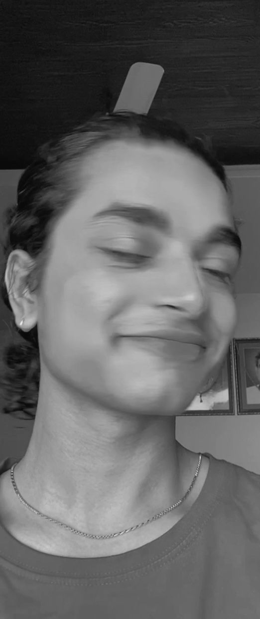 Una persona con una camiseta negra y pantalones de color claro está de pie en la cima rocosa de una montaña al atardecer, sosteniendo una cámara frente a su cara para tomar una foto. Un mar de nubes se extiende detrás de ellos, iluminado por la luz dorada del sol poniente.