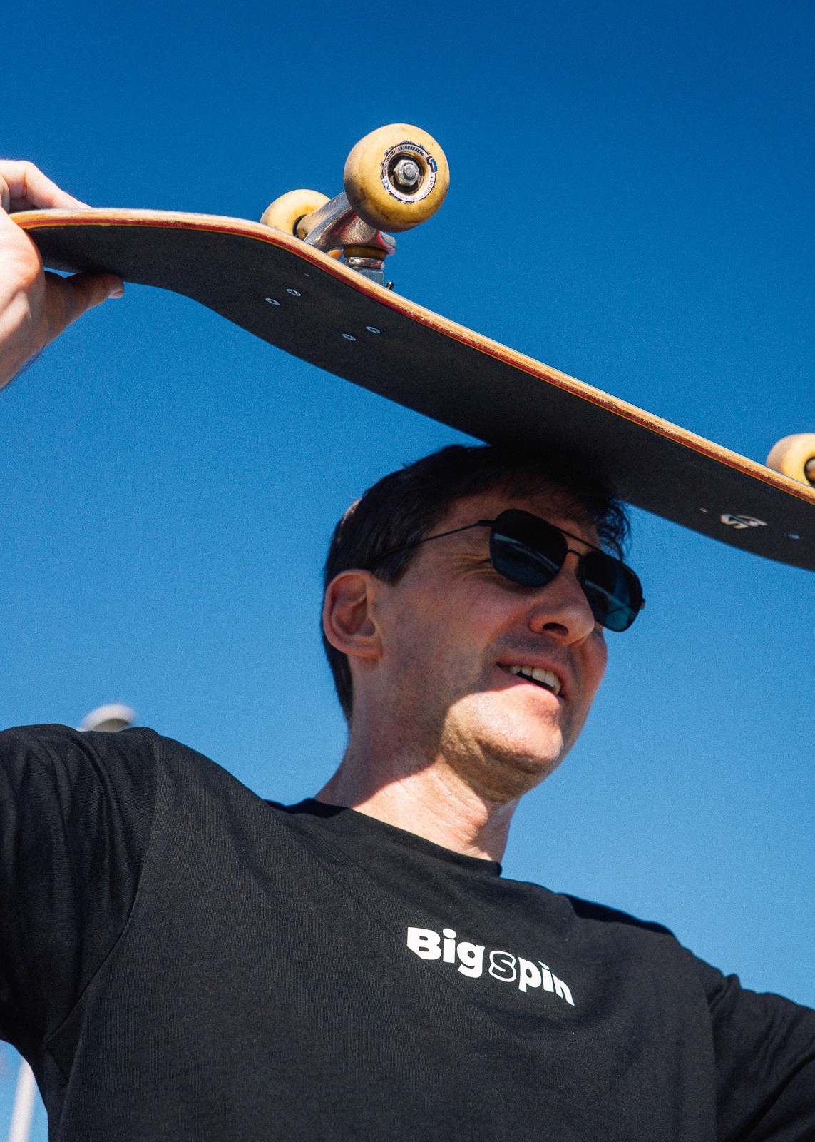 Chris, co-founder, holding a skateboard over his head outdoors