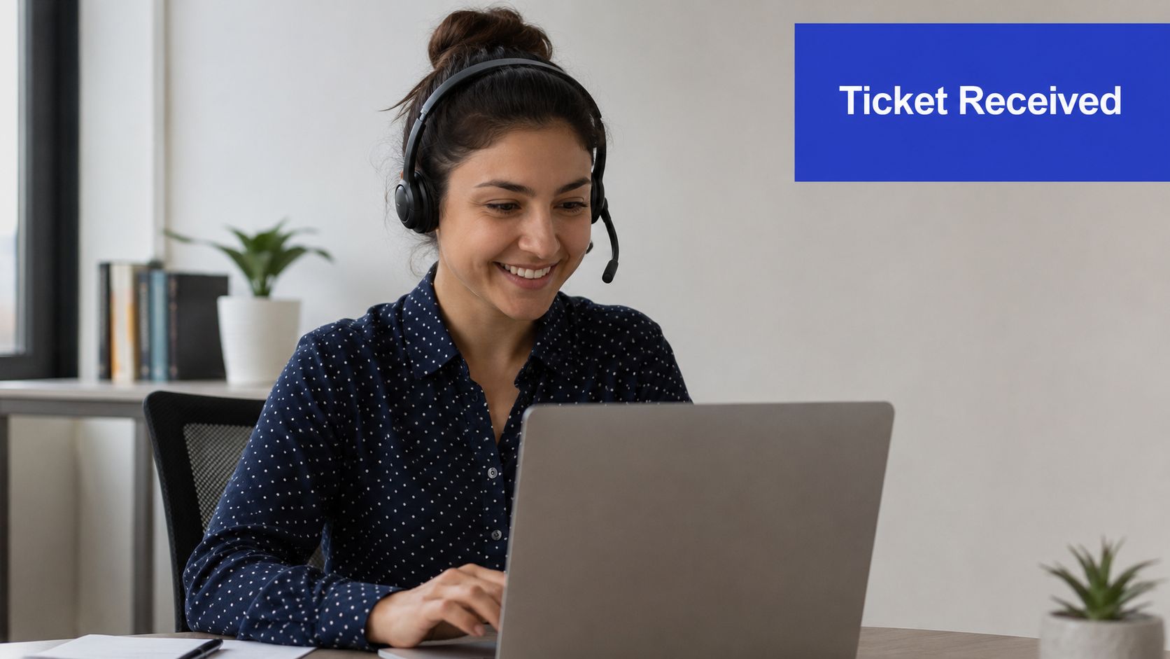 A smiling customer service representative wearing a headset and working on a laptop at her desk.