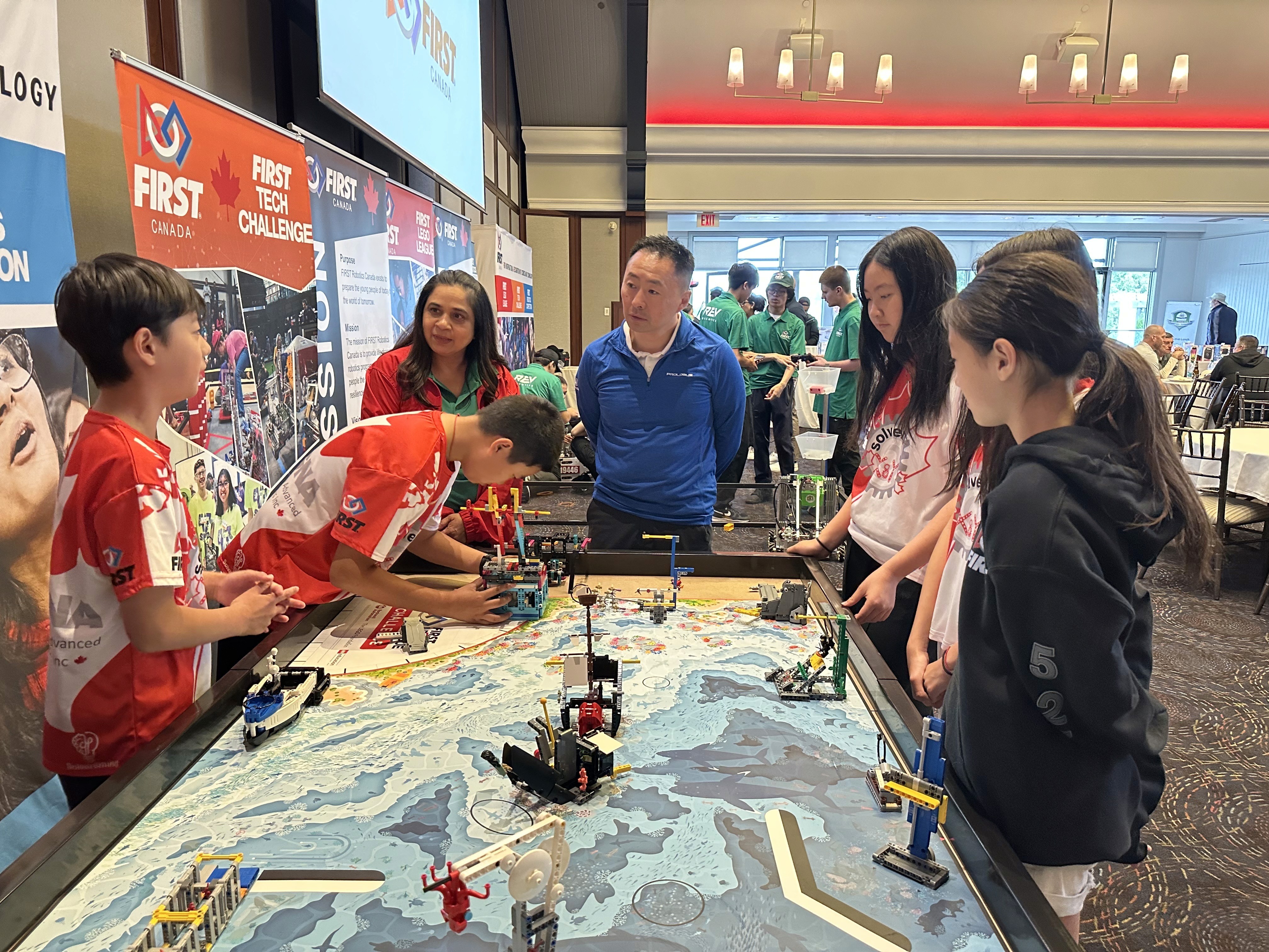 Samuel Pan from FLL Ontario Champion team Solvers of X & Y explains their Lego robot to Honda Canada Executive Steve Hui and FIRST Robotics Canada VP Arti.