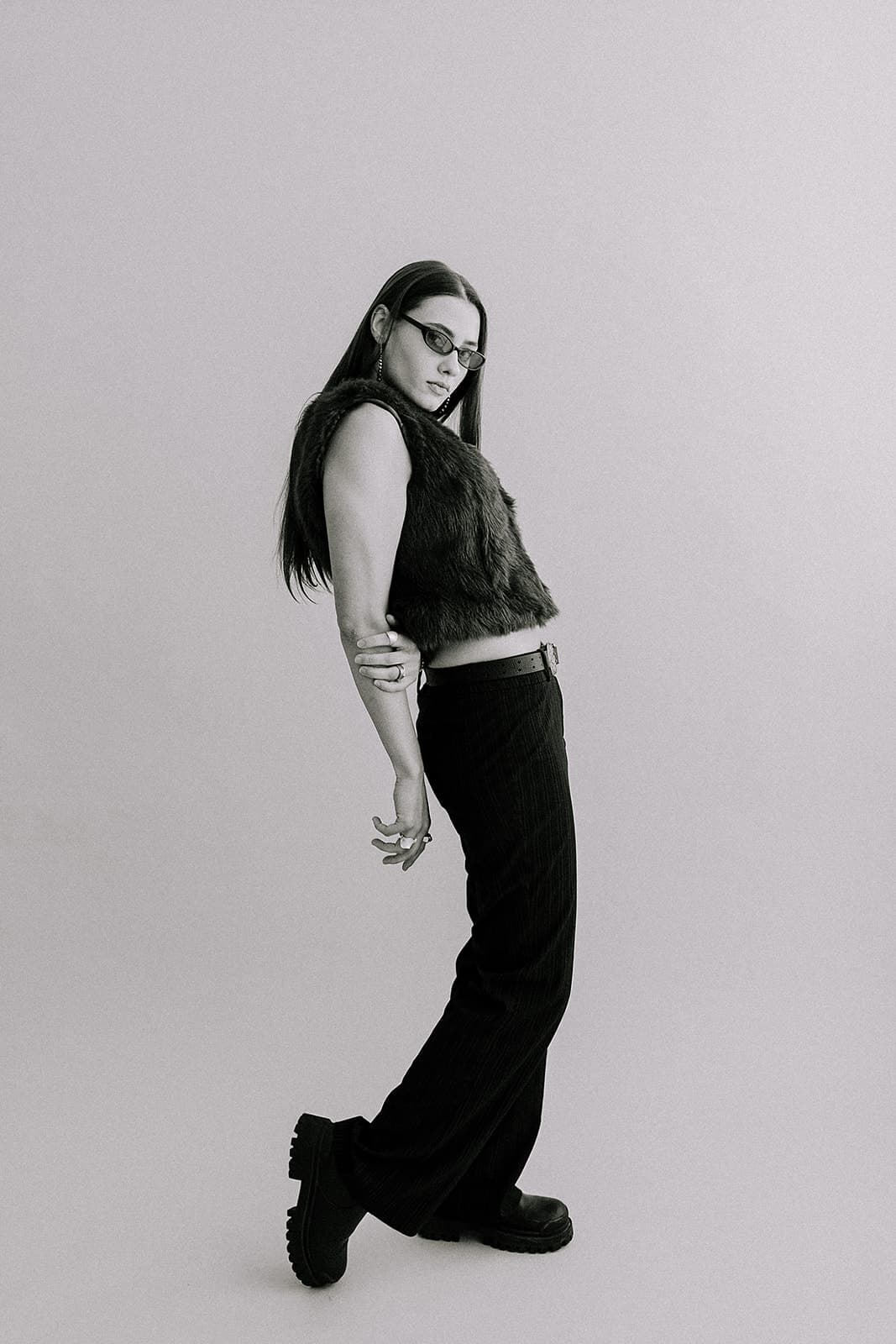 A model in a teal fur vest and black pants strikes a side profile pose in Revelator Studio, a photography studio in Shreveport with beautiful natural light.