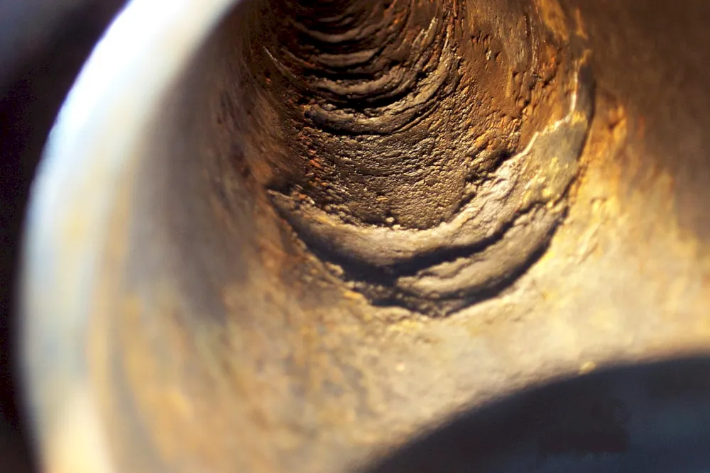 Close-up of the inside of a corroded metal pipe showing rust and damage to the surface.