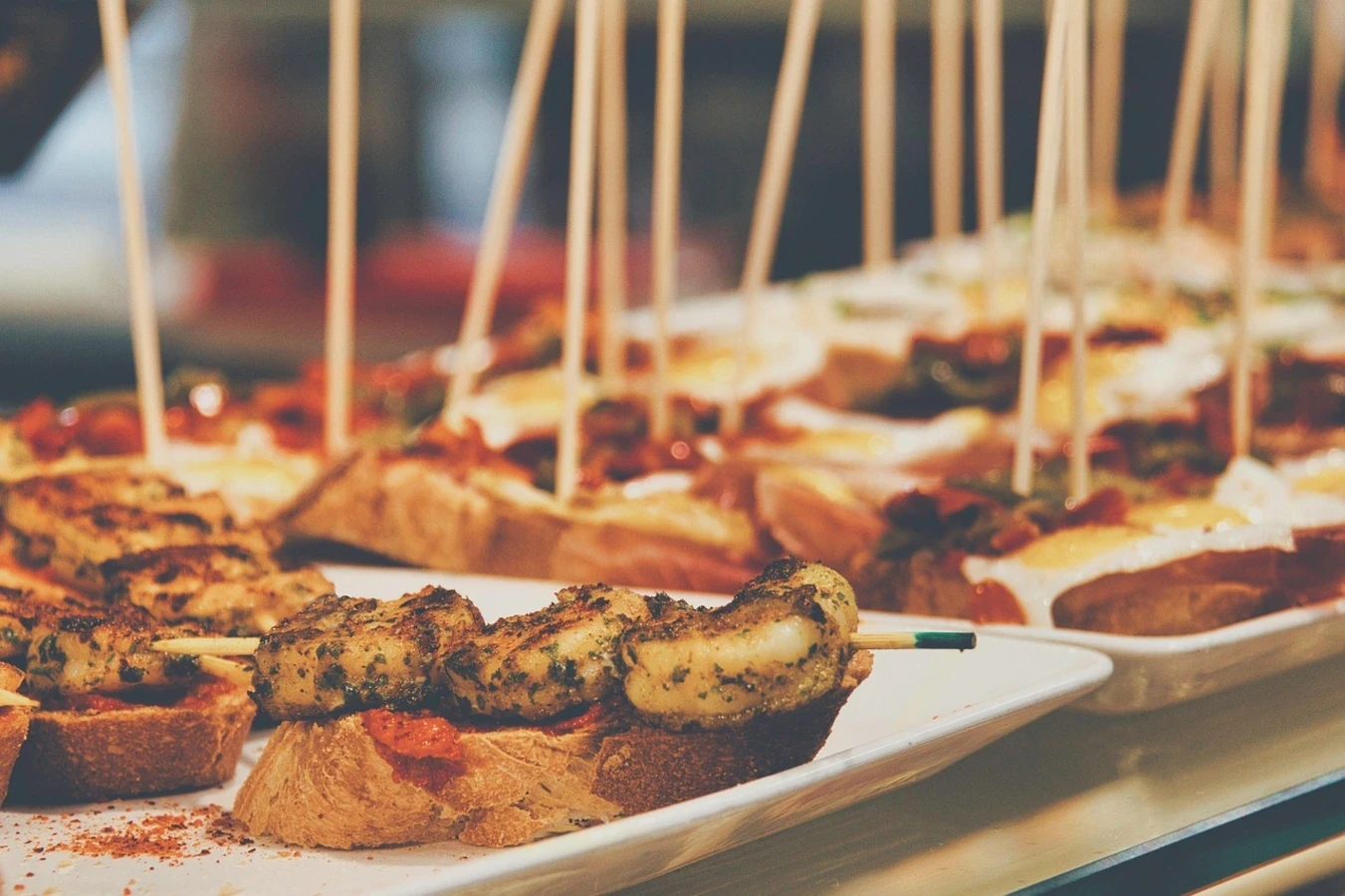 Learn the meaning of pinchos and pintxos, the ultimate Spanish bar snacks. Discover how to order, eat, and savor these delicious bites.