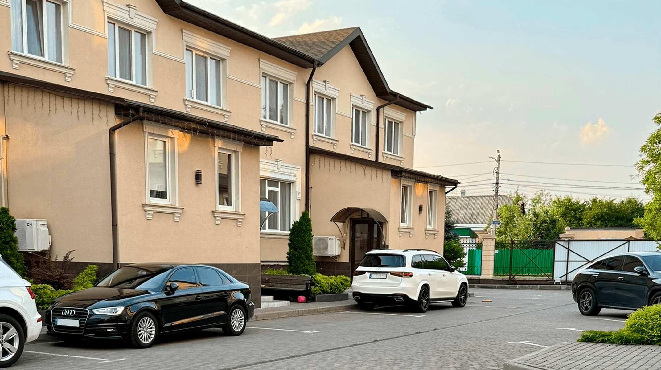 Фасад двоповерхового будинку з охайним подвір’ям та припаркованими автомобілями