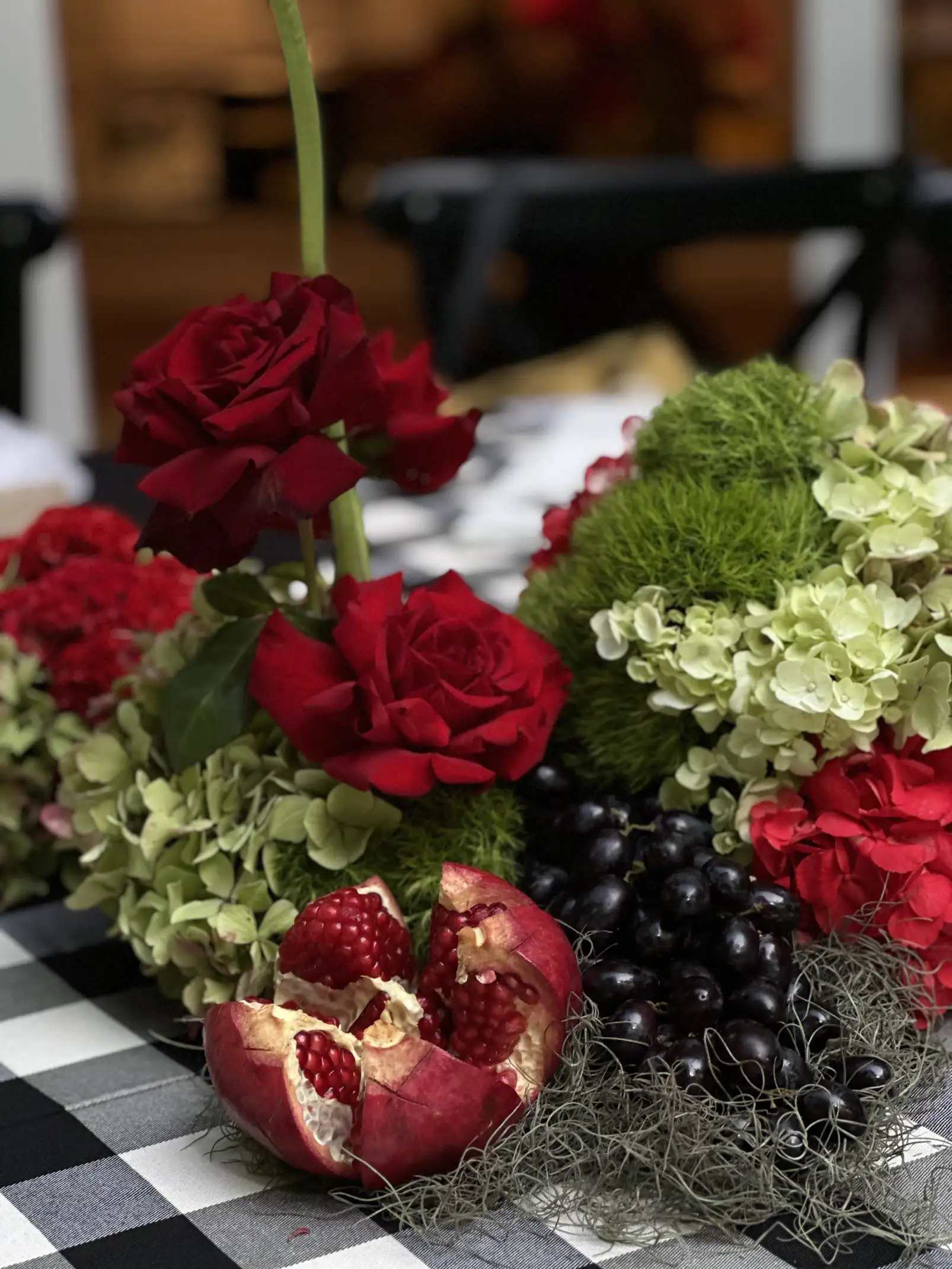 Arreglo floral con rosas rojas, hortensias verdes y granada abierta para decoración de mesa sofisticada con inspiración otoñal.