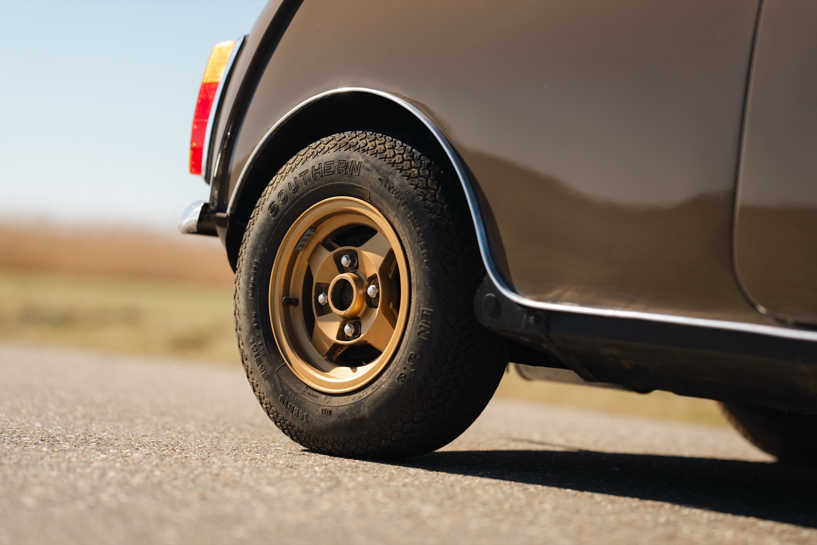 Close-up of a vehicle's rear wheel on a paved road, highlighting a gold-colored rim against a blurred background.