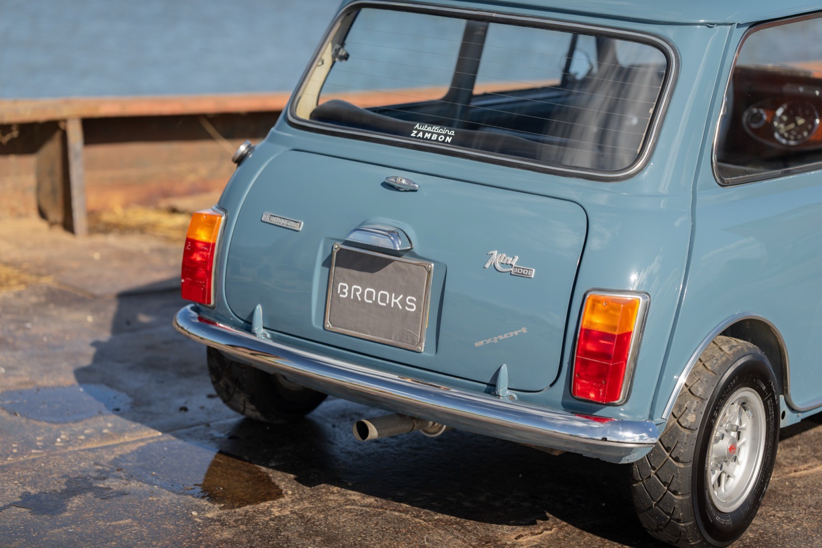 A vintage light blue car parked on a wooden dock, showcasing its rear and chrome details.
