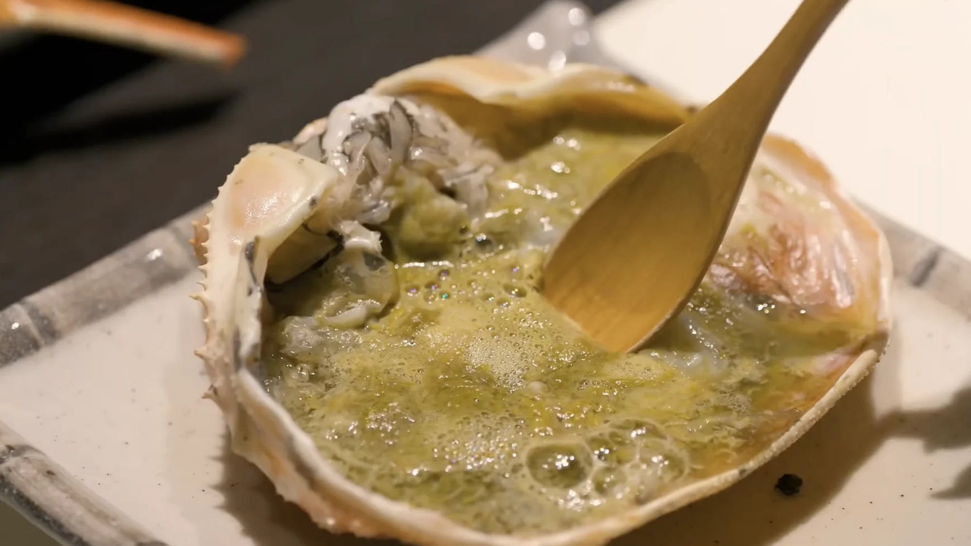 Crab miso being eaten from the shell with a wooden spoon.