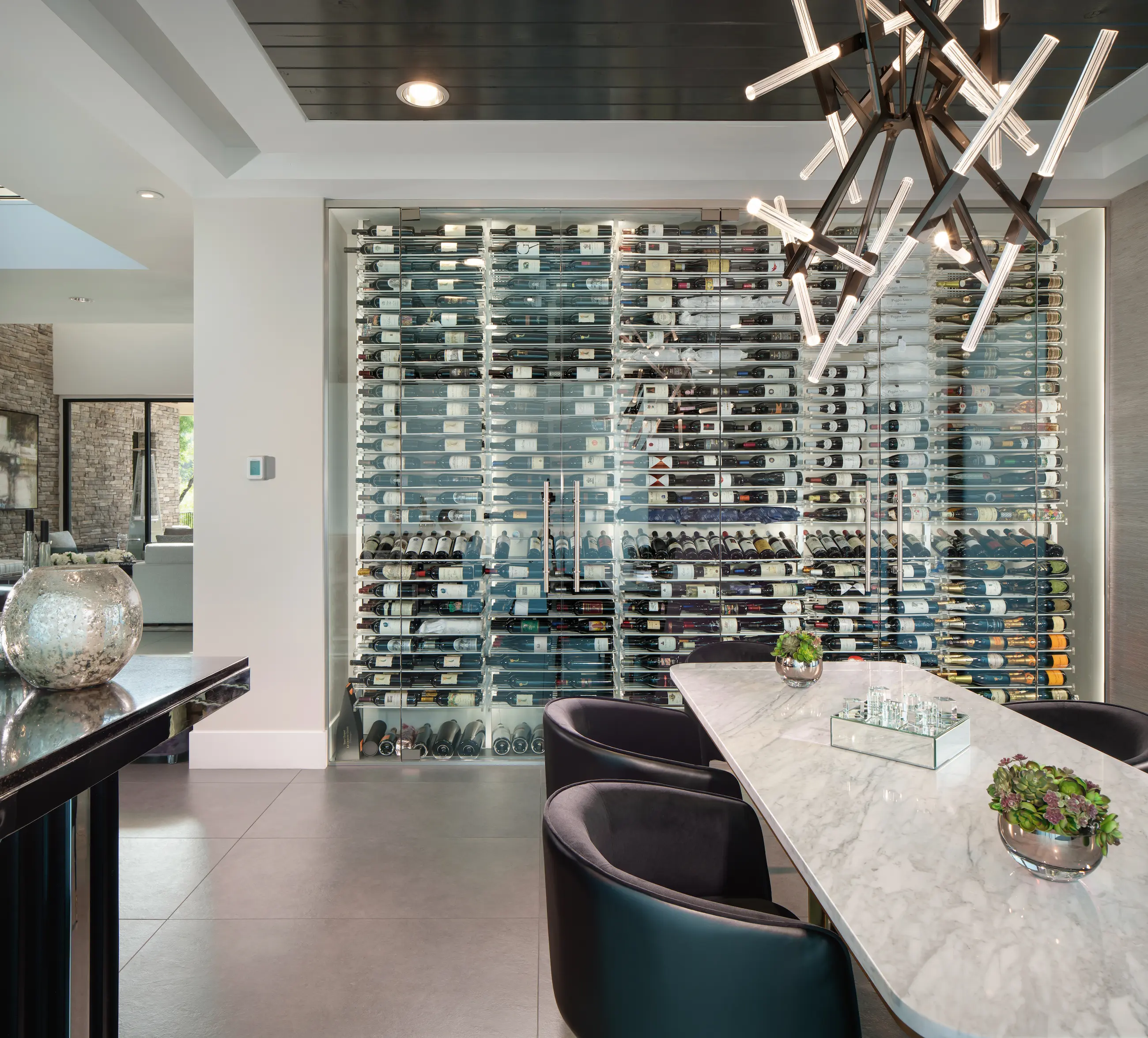 Modern glass-enclosed wine wall with black anodized metal racking and walnut shelving in a luxury dining room — custom wine cellar design by Innovative Wine Cellar Designs.