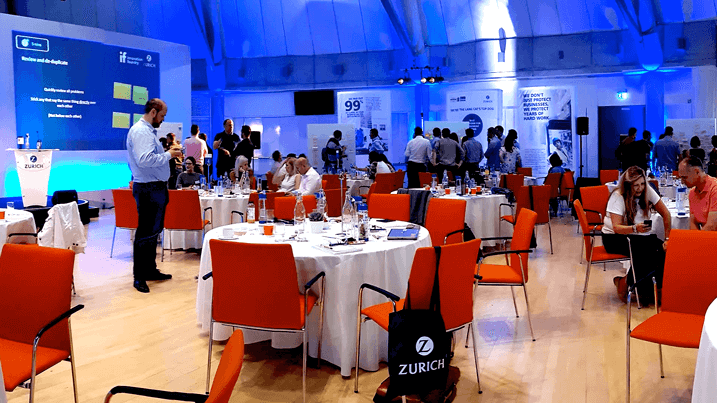 Corporate workshop event at Zurich Insurance with participants seated at round tables with red chairs