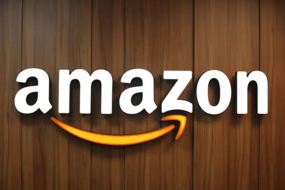 Amazon logo in bold white text with an orange arrow curved into a smile beneath, displayed on a wooden background.