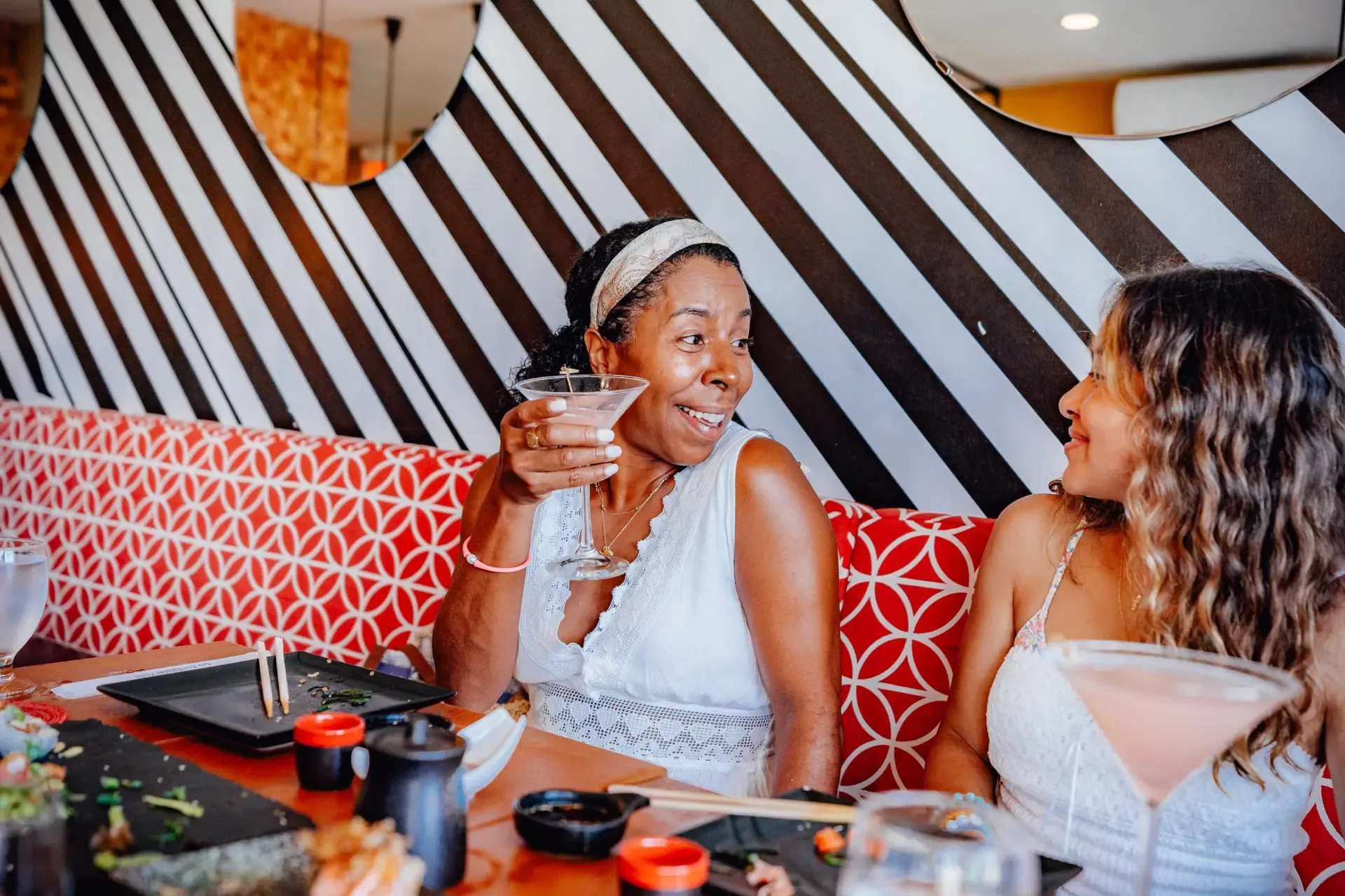 Smiling Nikkei server holding a platter of sushi rolls in a warmly lit dining setting