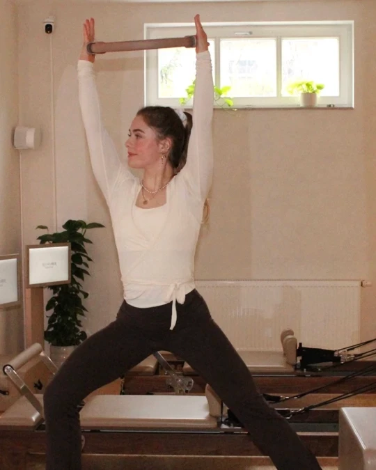 Frau liegt auf dem Reformer und hebt ein Bein senkrecht in die Luft – Reformer Pilates Übung im REFORMHER STUDIO Dresden