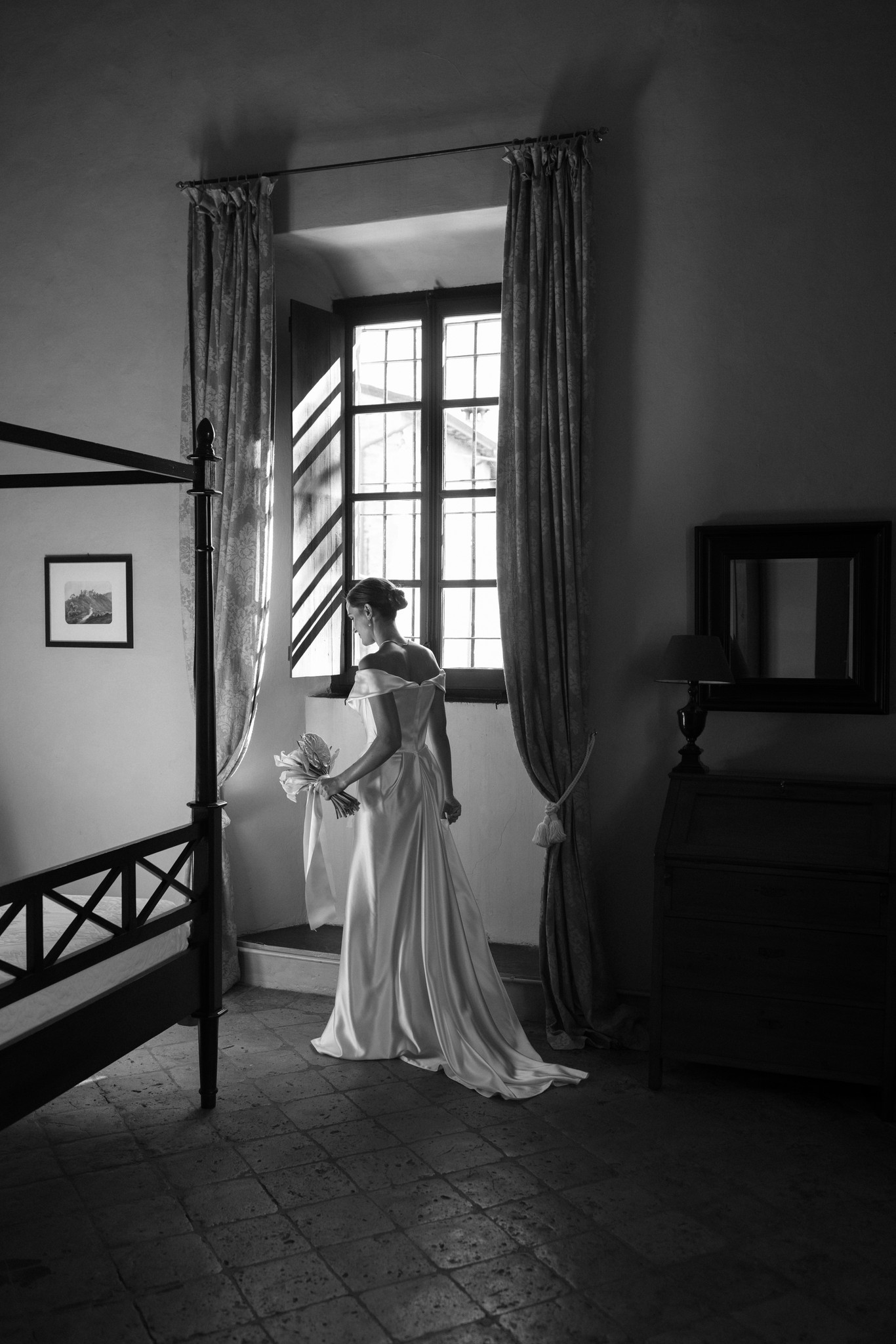 Sposa in abito bianco alla finestra del Castello di Scipione, luce naturale crea chiaroscuro, preparativi matrimonio