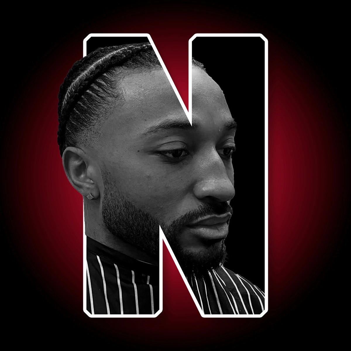 "N for Nice". Letter N with a picture of a clean cut gentleman still in a barbers cape. This gentleman is half in the N with the back of his head sticking out of the N. Behind the N is a red glow on a black background. 
