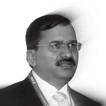 A happy corgi dog sits in front of yellow flowers.