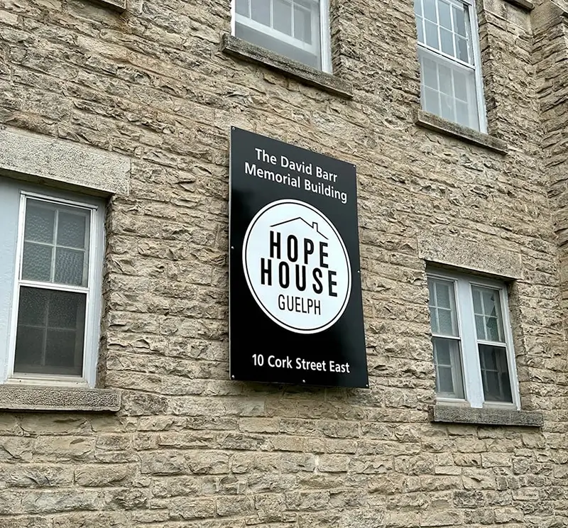 Sign on a stone building with the text "Moe's Pizza" displayed prominently, below two windows.