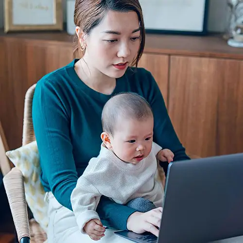 Mother holding her baby while using a laptop