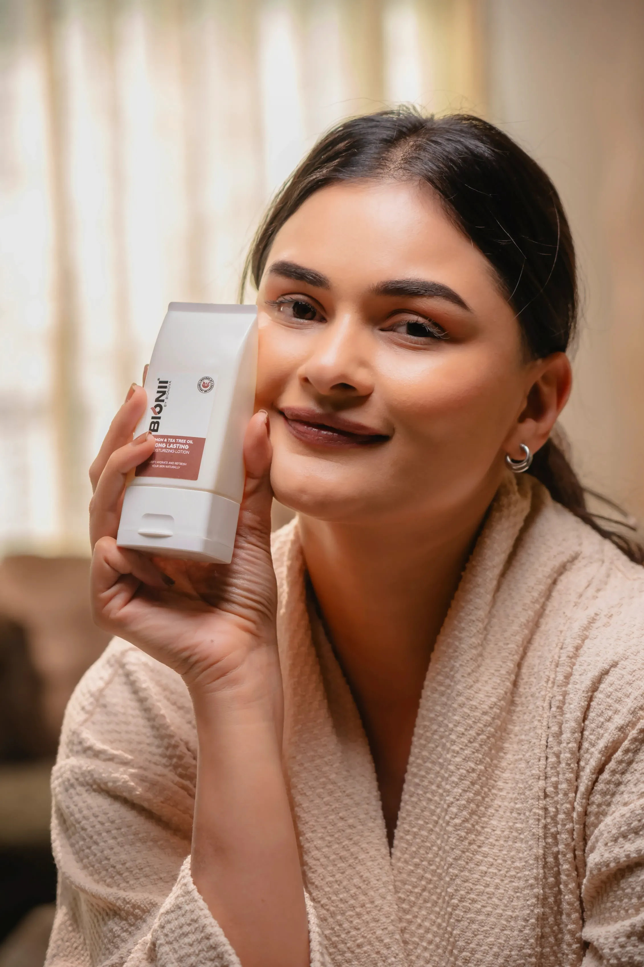 A smiling woman in a bathrobe holds up a can of beverage, with soft natural light and a cozy background.