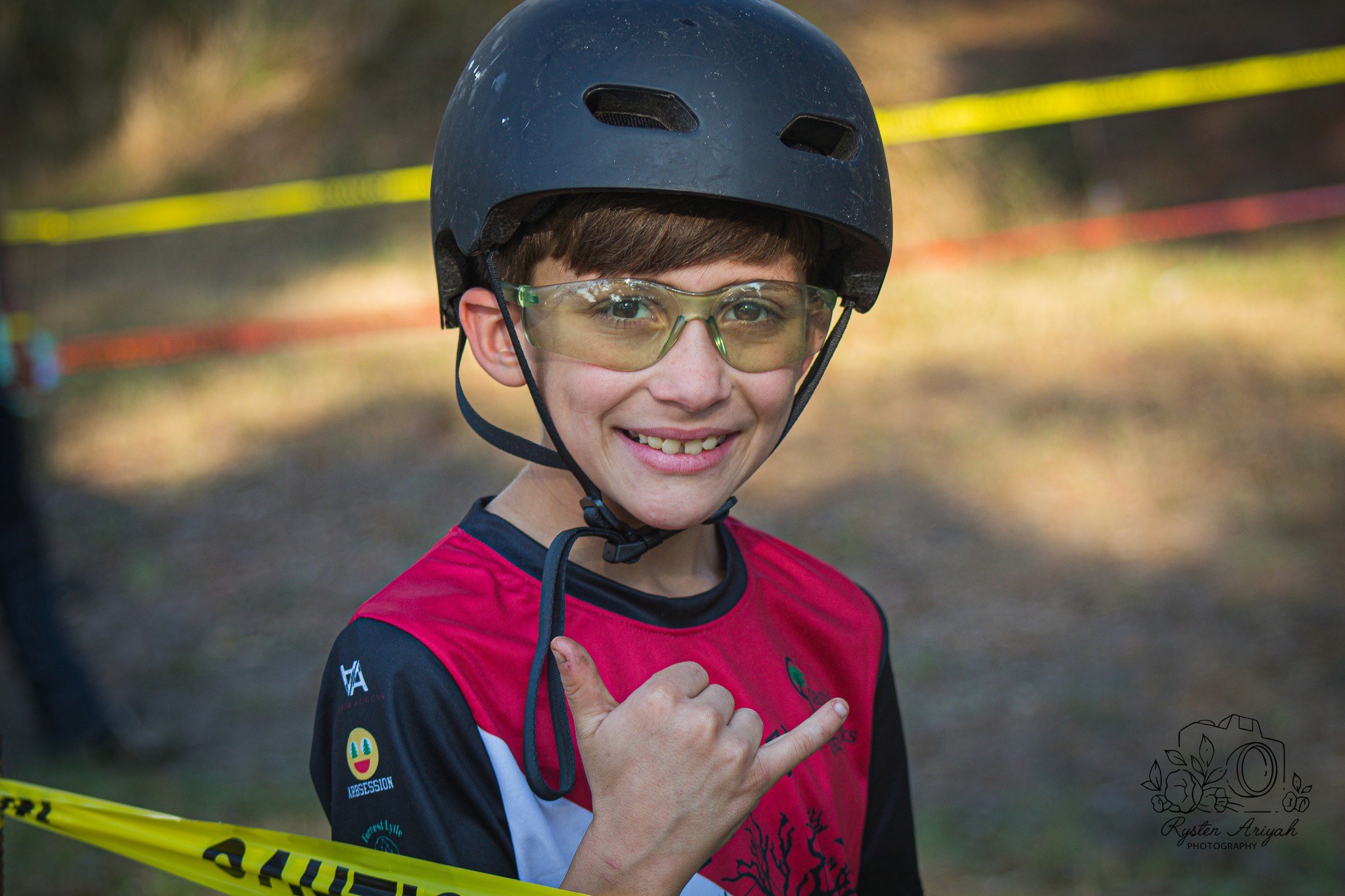 boy holding up hand in hang loose sign wearing a helment at kids climb area treeapalooza 2022