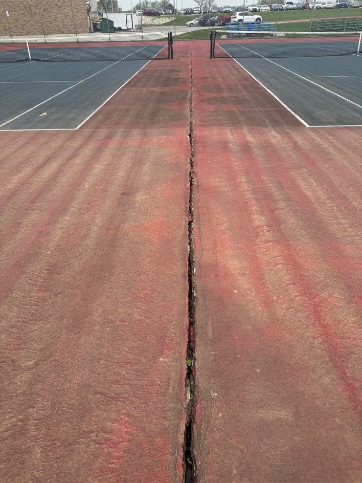 Worn tennis court with surface cracks and fading showing need for resurfacing