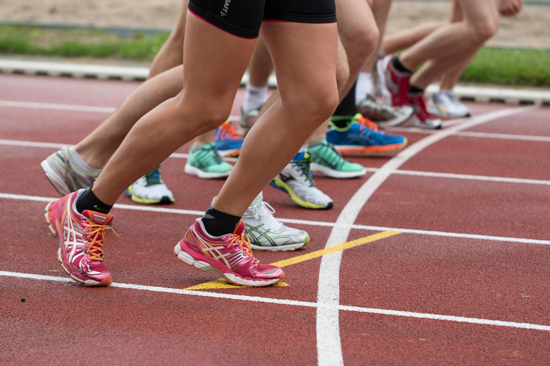 Close-up of runners' legs and colorful sneakers sprinting on a red track.