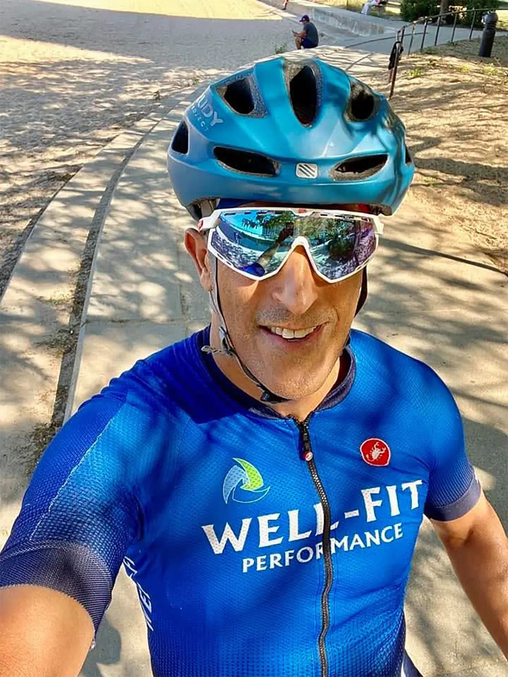 Well-Fit online triathlon coaching founder Sharone Aharon smiling during a bike training ride in his Well-Fit Performance cycling kit